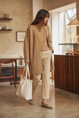 A camel coat over a beige knit and cream trousers, styled for a cafe